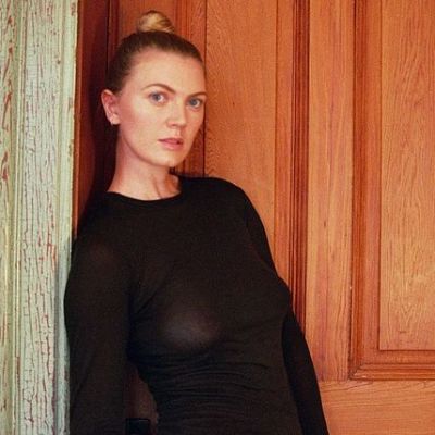 Ella Loudon is in a black dress and posing in front of a door.